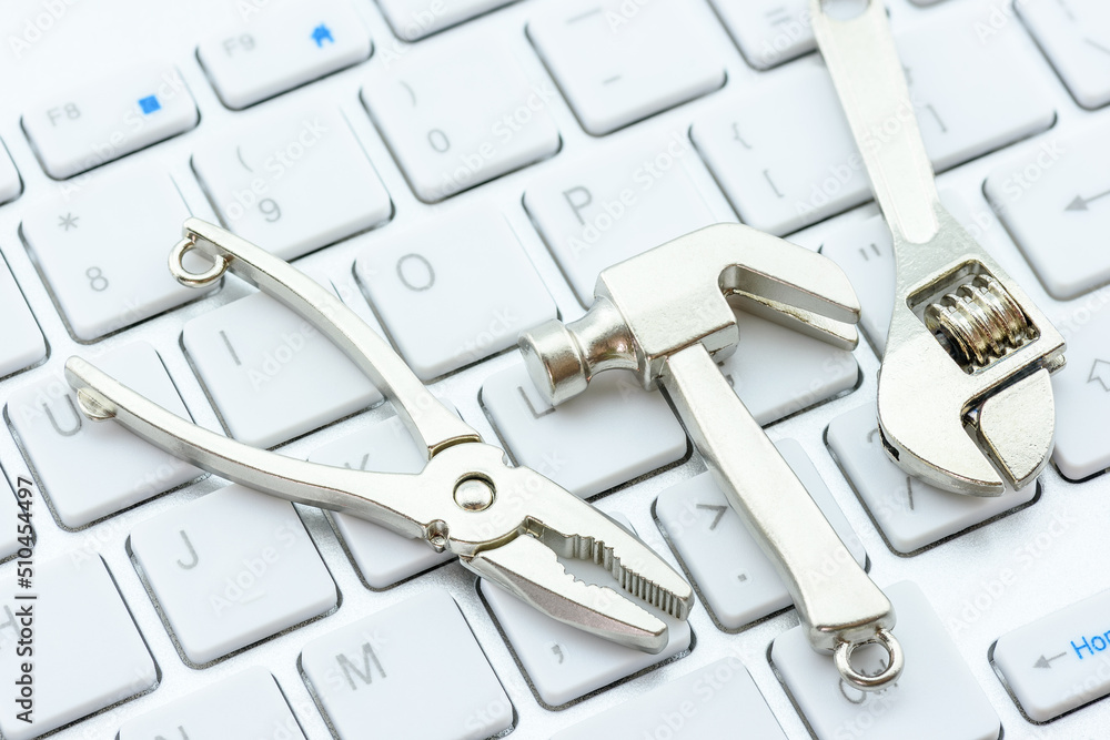 Fototapeta premium Computer hardware service and maintenance concept : Crest hammer, an adjustable wrench, a needle-nose plier on a computer keyboard, depicts repairing, software updating or changing to a newer version.
