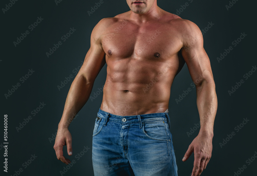 Muscle strong man guy in jeans on gray isolated background. Ideal fit body. Fashion portrait of strong brutal guy. Muscular sexy man with torso.
