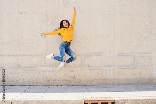 Happy asian woman jumping against conrete wall in the city photo