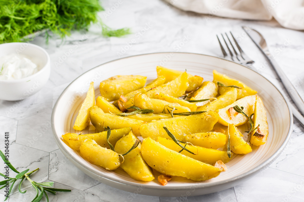 Baked potato wedges with garlic and rosemary on a plate on the table. Homemade vegetarian dish Baked potato wedges with garlic and rosemary on a plate on the table. Homemade vegetarian dish