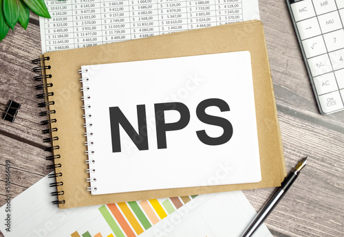 On a wooden background, a white notebook with the inscription NPS Net Promoter Score