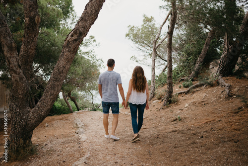 Canvas Print A photo from behind of a Hispanic man and his Latina girlfriend who are descending from the wooded hill to the sea in a highland park in Spain