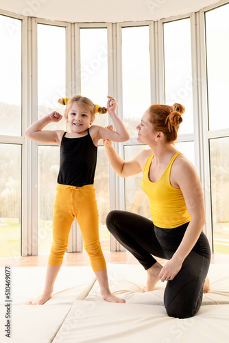 Young fit mom and her daughter in matching clothes, showing muscles.