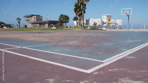 Palm trees and basketball sport field or court on beach, California coast, USA. Streetball playground on shore and lifeguard stand, tower ot station. Mission beach, San Diego. Hoop, backboard and sky.