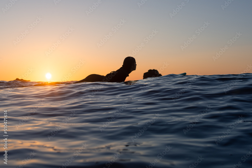 Low angle view of a surfer girl seen from behind. Paddling on a board in the water