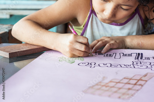 close-up of a brown latina girl  coloring with her colored pencils a hand drawn picture. poor girl of limited economic resources making a billboard. concept of poverty