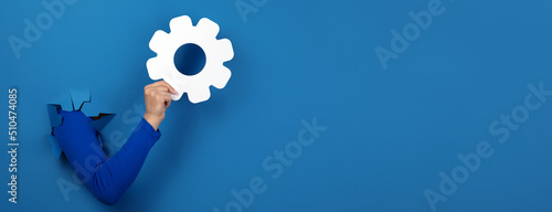 hand holding gear symbol over blue background, panoramic layout