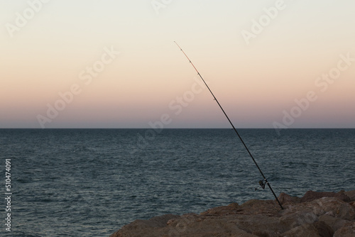 Fishing rod sticks out of jetty rocks at sunset © Mark