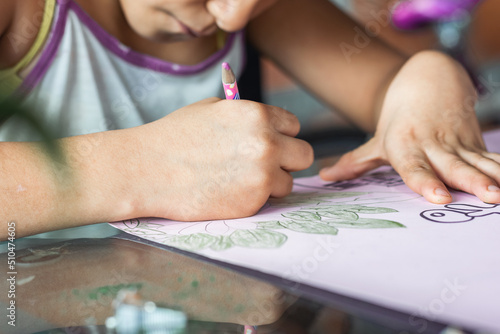 detailed view of a hand of a brown-skinned, low-income latina girl coloring with her colored pencils on a pink poster. girl concentrating on studying and drawing. concept of a poor person.