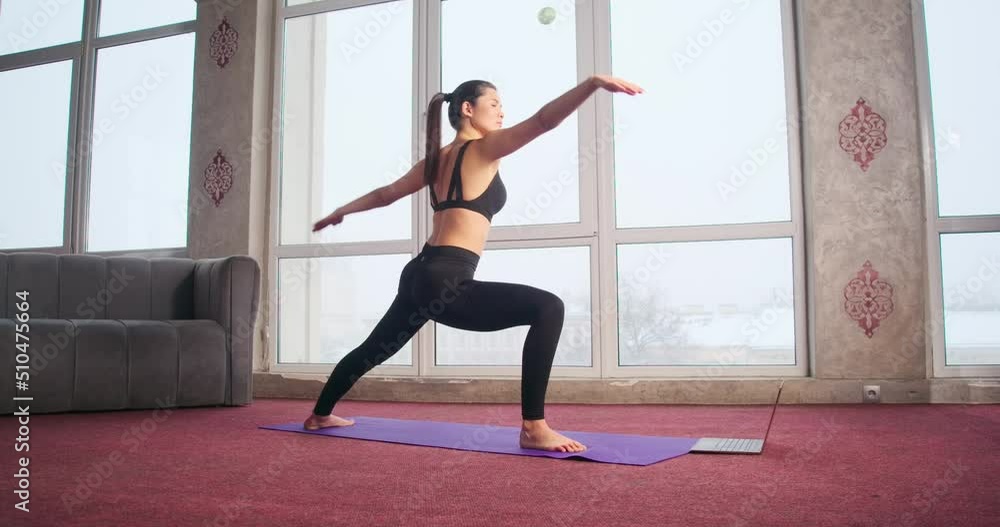 Side view of brunette girl with ponytail standing on yoga mat, making lunges, raising hand, bending. Pretty, slim female doing yoga, exercising indoors. Concept of new age. Side view of brunette girl with ponytail standing on yoga mat, making lunges, raising hand, bending. Pretty, slim female doing yoga, exercising indoors. Concept of new age.