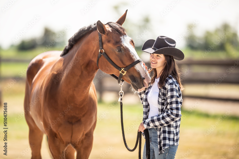 Fototapeta premium A bond between a horse and a young woman in cowboy hat on a ranch outdoors