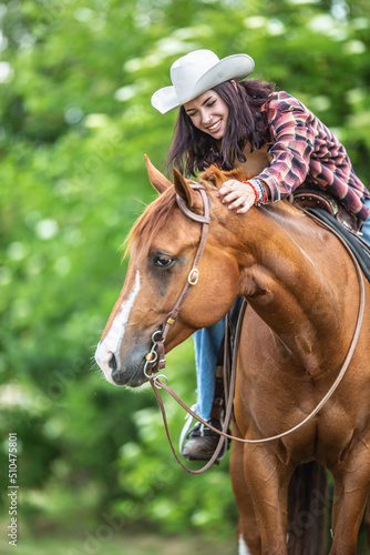 Good looking girl laughs and pats the brown horse during a summer ride in the nature