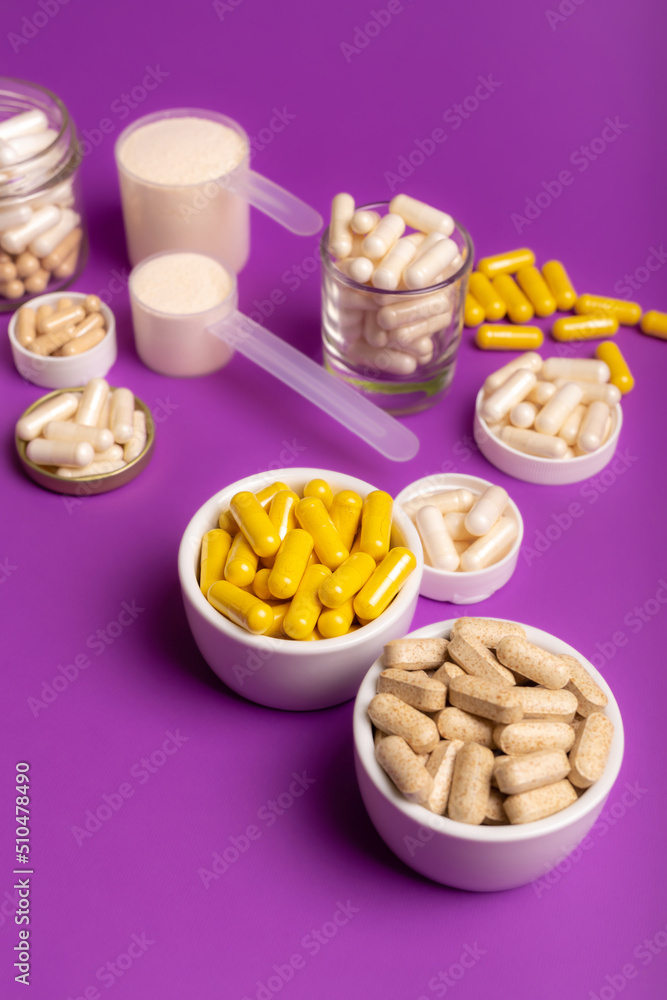 Multivitamin capsules and minerals to support to maintain a high level of human immunity and good health. Composition with organic food supplements on purple background from above. Multivitamin capsules and minerals to support to maintain a high level of human immunity and good health. Composition with organic food supplements on purple background from above.