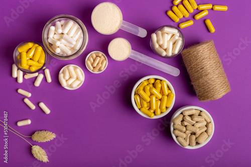 Multivitamin capsules and minerals to support to maintain a high level of human immunity and good health. Composition with organic food supplements on purple background from above.