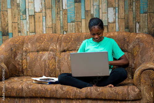 young black african hipster girl working from home sitting on a sofa using laptop computer. business woman shopping online at home photo
