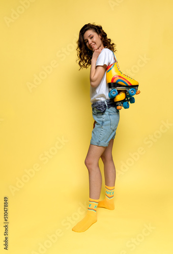 A young lady with rainbow quad rollers on yellow background
