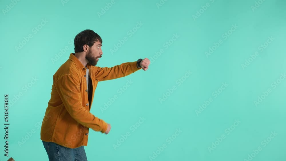 Close-up of expressive bearded guy looking at wrist watch, showing hurry while screaming and running on one spot isolated against blue studio background. Portrait of male rushing to sale and discounts Close-up of expressive bearded guy looking at wrist watch, showing hurry while screaming and running on one spot isolated against blue studio background. Portrait of male rushing to sale and discounts