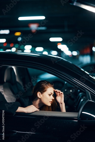vertical photo from the side, at night, of a woman sitting in a black car and looking out of the window looking into the side view mirror holding her hand near her face © SHOTPRIME STUDIO