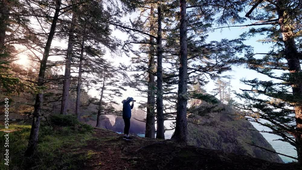 Man stands at the top of steep slope with lush fall grove around. Photographer takes pictures of pristine, beautiful wilderness with dense fir forest and seascape around. High quality 4k footage Man stands at the top of steep slope with lush fall grove around. Photographer takes pictures of pristine, beautiful wilderness with dense fir forest and seascape around. High quality 4k footage