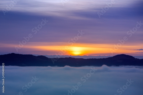 Foggy clouds fell below mountain level at sunrise, orange horizon, violet