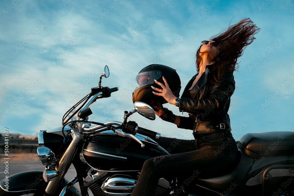 Amazing scene, Attractive young woman taking of motorcycle helmet and tossing her hair in the sunset on the open road 