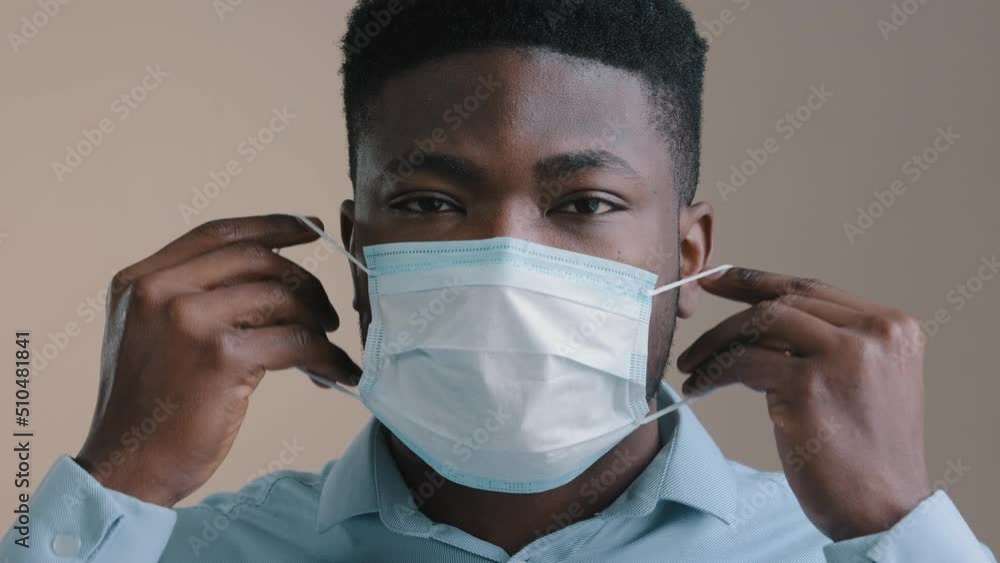Close up male african businessman american adult man put medical mask on face protect individual respirator from coronavirus viral infection cover mouth nose look at camera stop world pandemic concept Close up male african businessman american adult man put medical mask on face protect individual respirator from coronavirus viral infection cover mouth nose look at camera stop world pandemic concept