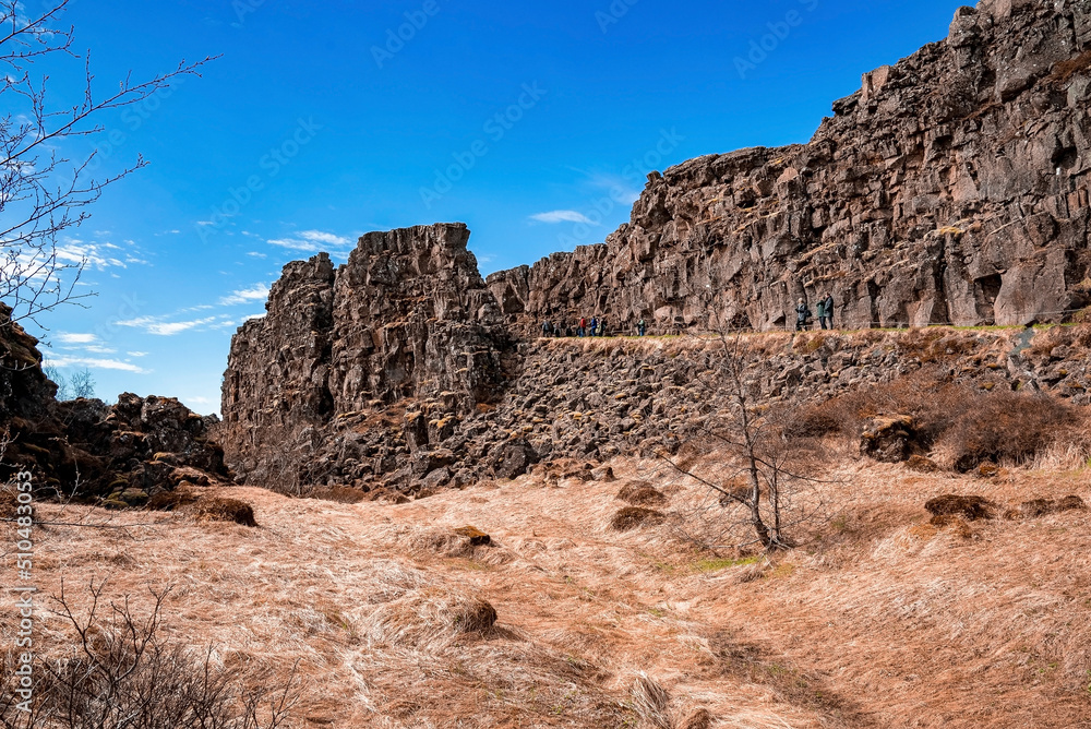 Tourists exploring beautiful volcanic landscape. People are standing by rock formation against sky during sunny day. Concept of tourism at dramatic land in northern Alpine region.