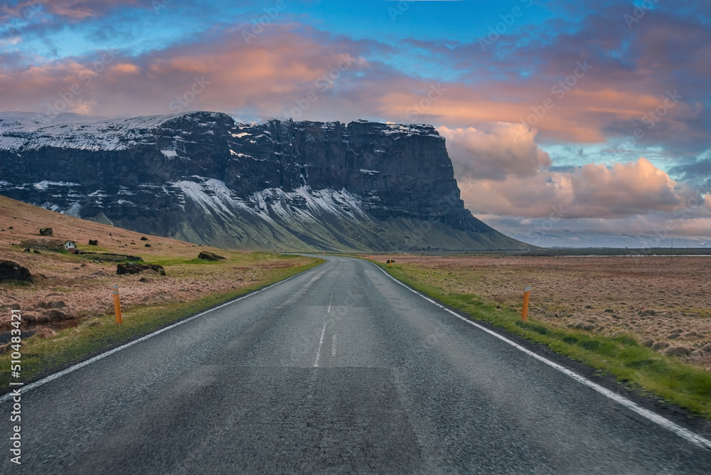 Naklejka premium Diminishing highway leading towards mountain. Empty road against cloudy sky during sunset. Scenic view of street amidst volcanic landscape during stormy weather.