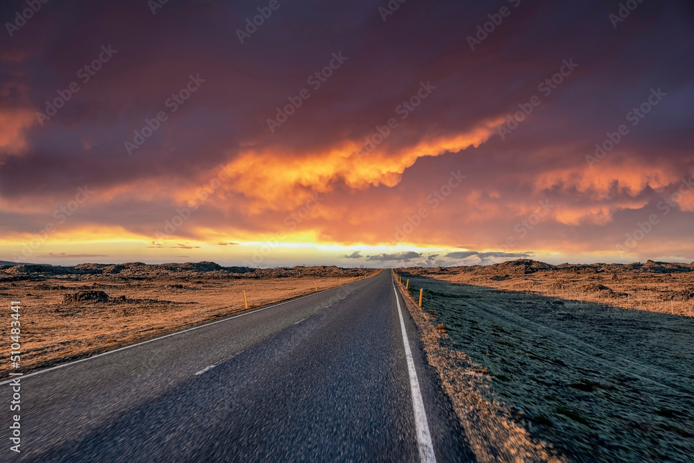 Empty highway amidst volcanic landscape. Diminishing road against dramatic sky during sunset. Scenic view of street in northern Alpine region during stormy weather.