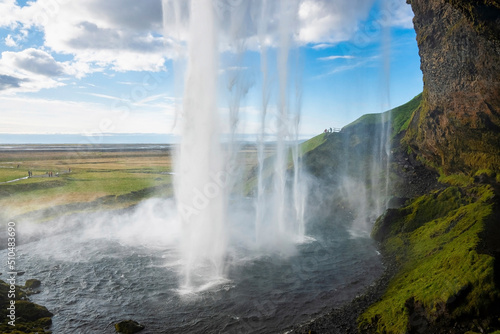 Scenic cascades of Seljalandsfoss flowing from mountain. Majestic beautiful waterfall against blue cloudy sky. Close-up idyllic view of famous tourist attraction in valley.