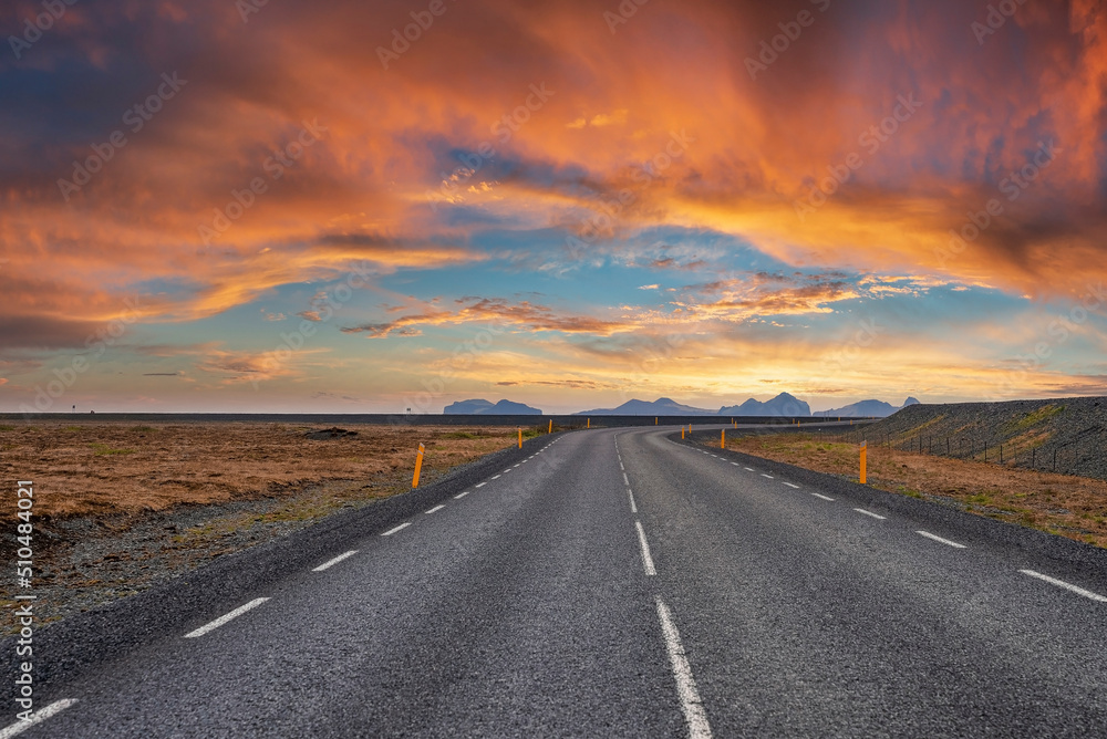 Diminishing empty road amidst volcanic landscape. Road markings on street on mountain against cloudy sky. Scenic view of highway with yellow poles on roadside during sunset.