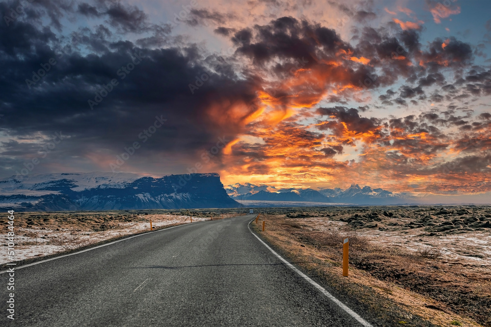 Empty road amidst volcanic landscape by mountain during stormy weather. Diminishing street against dramatic sky. Scenic view of highway in valley during sunset.