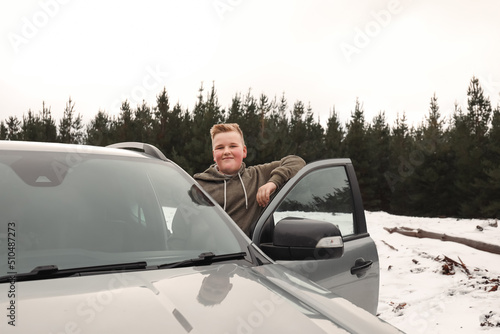 Happy preteen boy standing on side of vehicle smiling in the snow on cold winter drive at Shooters Hill, NSW Australia