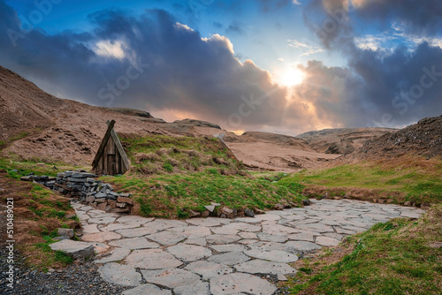 Beautiful Turf house and geothermal hot spring in Hrunalaug. Sun shining through clouds over moss covered structure amidst rocks. Idyllic scenery of mountains against sky during sunset. photo