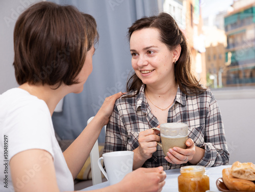 Portrait of young woman talking with mature woman, with cup of coffee at table