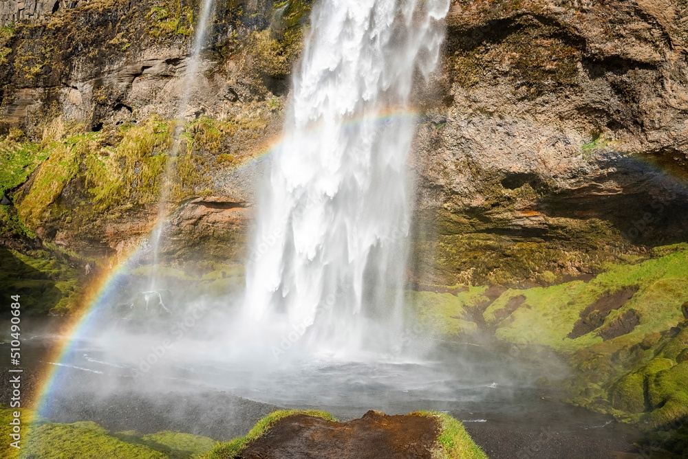 Obraz premium Beautiful rainbow at Seljalandsfoss flowing from mountain. Scenic waterfall with mist in river. Idyllic view of famous attraction in valley of northern Alpine region.