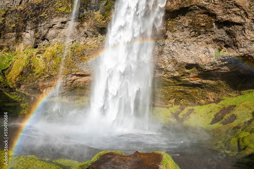 Beautiful rainbow at Seljalandsfoss flowing from mountain. Scenic waterfall with mist in river. Idyllic view of famous attraction in valley of northern Alpine region.