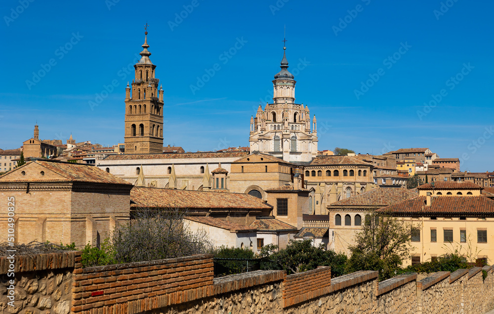 View of bell tower and dome of ancient Roman Catholic Cathedral rising above old residential buildings of historic quarter of Tarazona city against blue cloudless sky on sunny spring day, Spain..