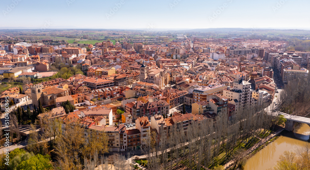 Scenic drone view of modern residential areas of Aranda de Duero city on banks of Duero river on sunny spring day on background of natural rural landscape, Burgos, Spain