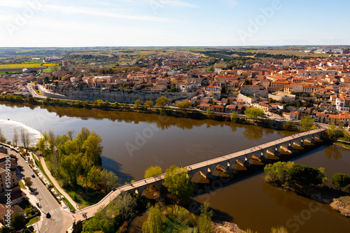 Picturesque aerial view of Zamora city overlooking brownish tiled roofs of residential buildings and ancient arched bridge over Duero river on spring day  Spain