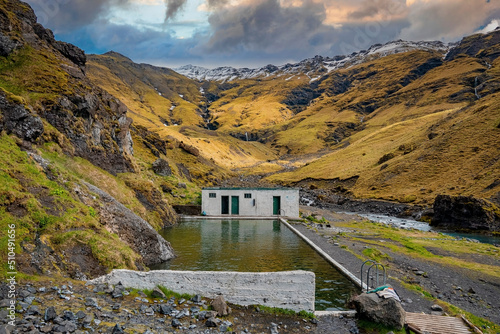 Scenic geothermal Seljavallalaug against green mountain range. Beautiful natural hotspring pool against cloudy sky. Idyllic view of oldest swimming pool in valley during sunset. photo