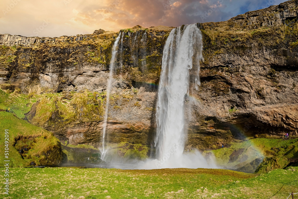 Beautiful Seljalandsfoss flowing from mountain. Majestic wonderful waterfall against cloudy sky. Scenic view of famous tourist attraction in valley during sunset.