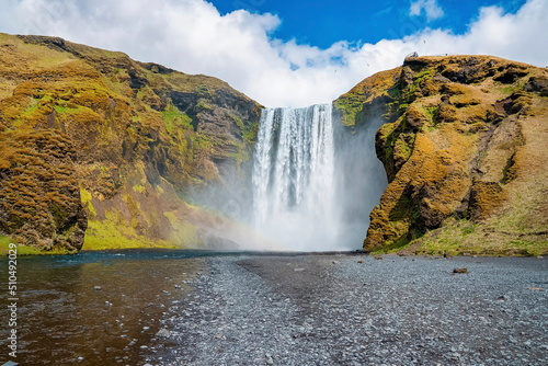 Powerful cascades of Skogafoss waterfall in valley. Beautiful river water flowing amidst cliffs against blue sky. Idyllic natural scenery of volcanic landscape.