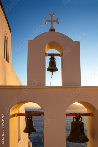 The bell tower of white church on Santorini island during orange sunset.