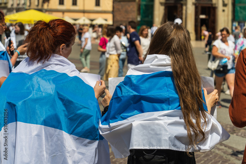 Russian activists wearing a white-blue-white flag on their backs on a sunny day participate in an anti-war protest in a European country against the Russian invasion of Ukraine