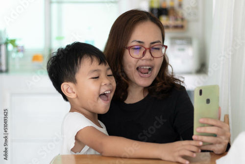 Mother's day and family concept. Asian beautiful Mother and child happily beautiful young mom and cute little boy are sitting together at home, using a smart phone and smiling and taking Selfie.