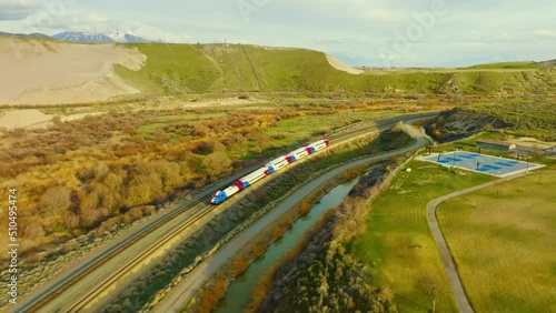 AERIAL - Train on railroad tracks next to river near Bluffdale, Utah, forward tracking photo
