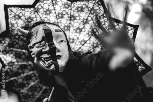 Portrait of sexy and young japanese woman with beautiful old traditional black kimono, traditional double mask (of 'hannya' and 'noh') and lace sun umbrella in the autumn forest (in black and white)