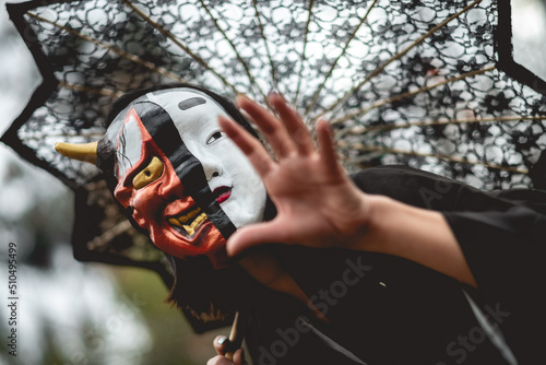 Portrait of sexy and young japanese woman with beautiful old traditional black kimono, traditional double mask (of 'hannya' and 'noh') and lace sun umbrella in the autumn forest 