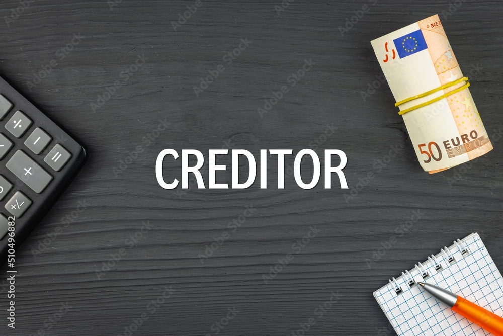 CREDITOR - word (text) and euro money on a wooden background, calculator, pen and notepad. Business concept (copy space).